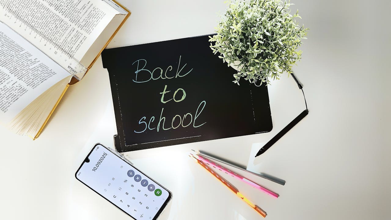 A bright, organized workspace for back to school featuring books, a phone, a plant, and stationery.