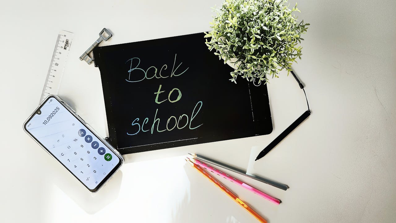 Aerial view of school supplies including a blackboard with 'Back to School' text, smartphone, and pens.